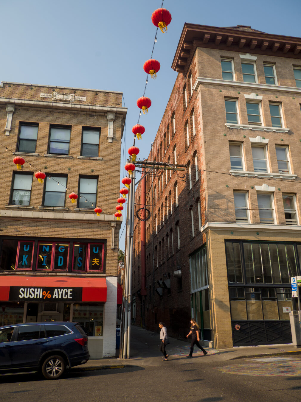 A string of red lanterns and light bulbs appears to be between two old mid-rise buildings. In the building on the left, there's a sushi restaurant on the first floor and a children's Kung Fu school on the second floor.