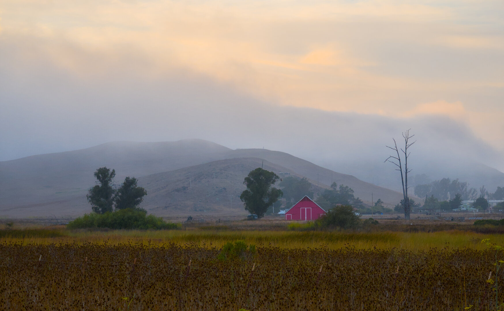 Farmland with a red barn and a few trees was framed by the mighty clouds stained golden by the setting sun