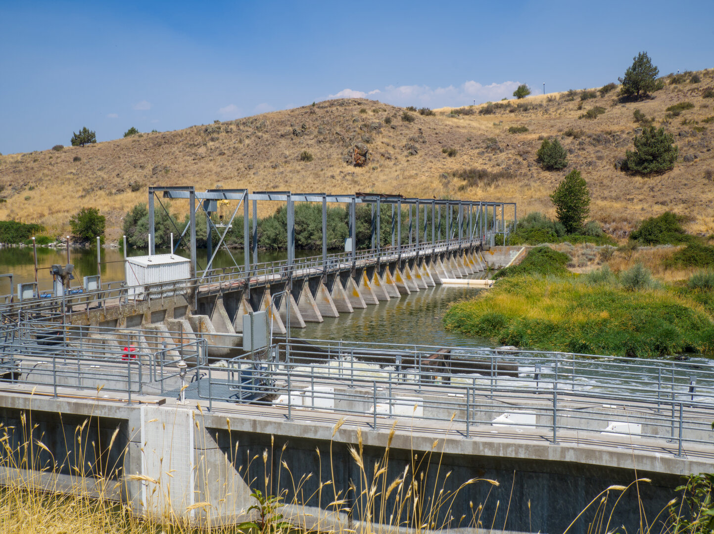 Concrete dam with steel fencing on top leading to an arid hill