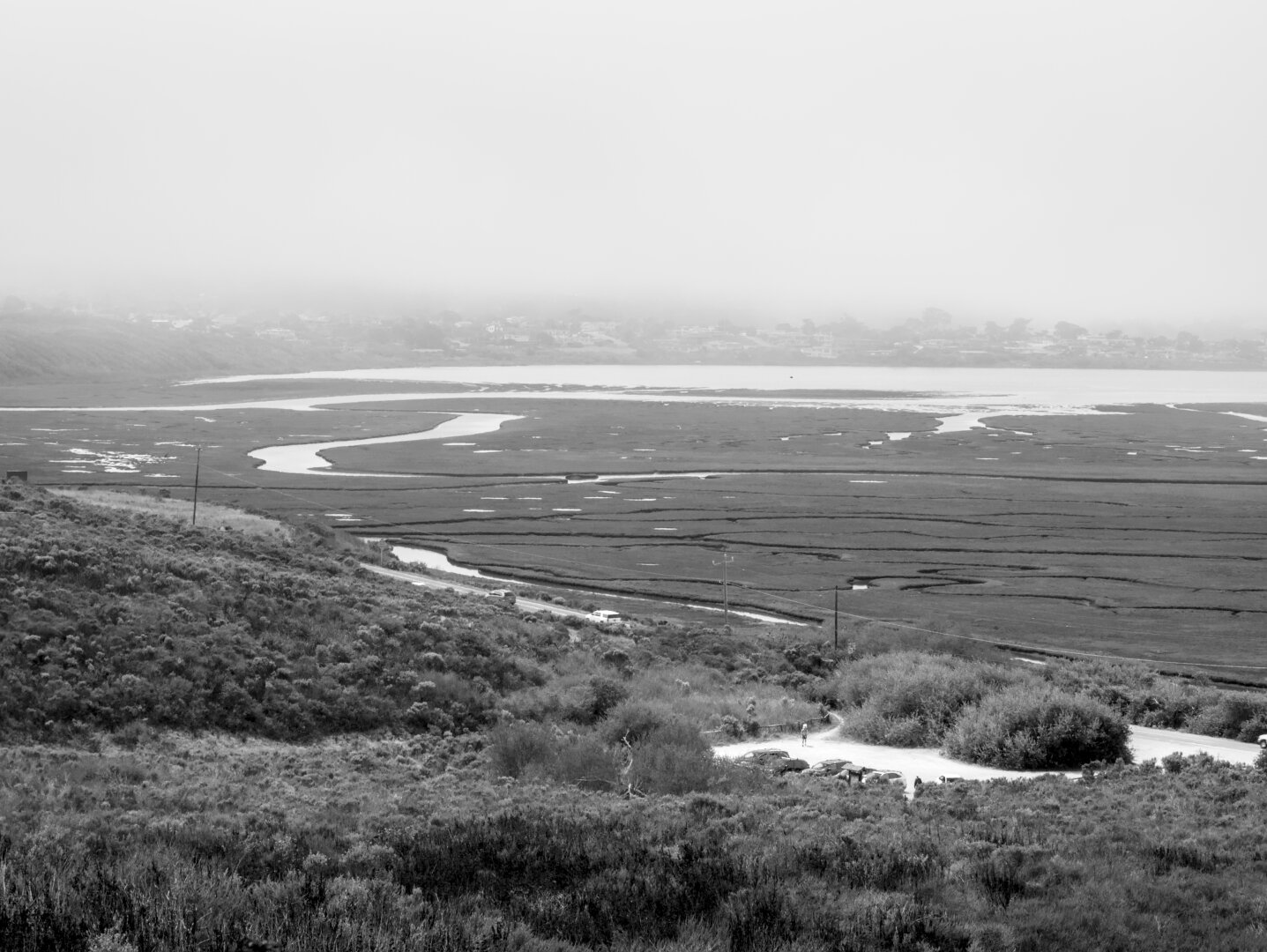 Looking down at the foggy wetland from a hill, showing a parking lot in the foreground