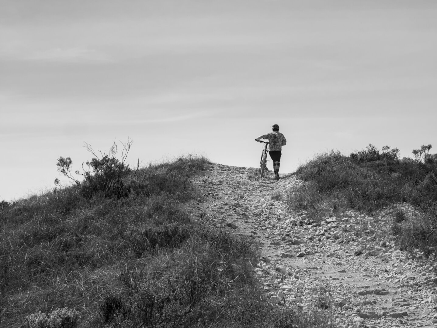A person was walking a mountain bike up a very steep and rocky trail towards the peak