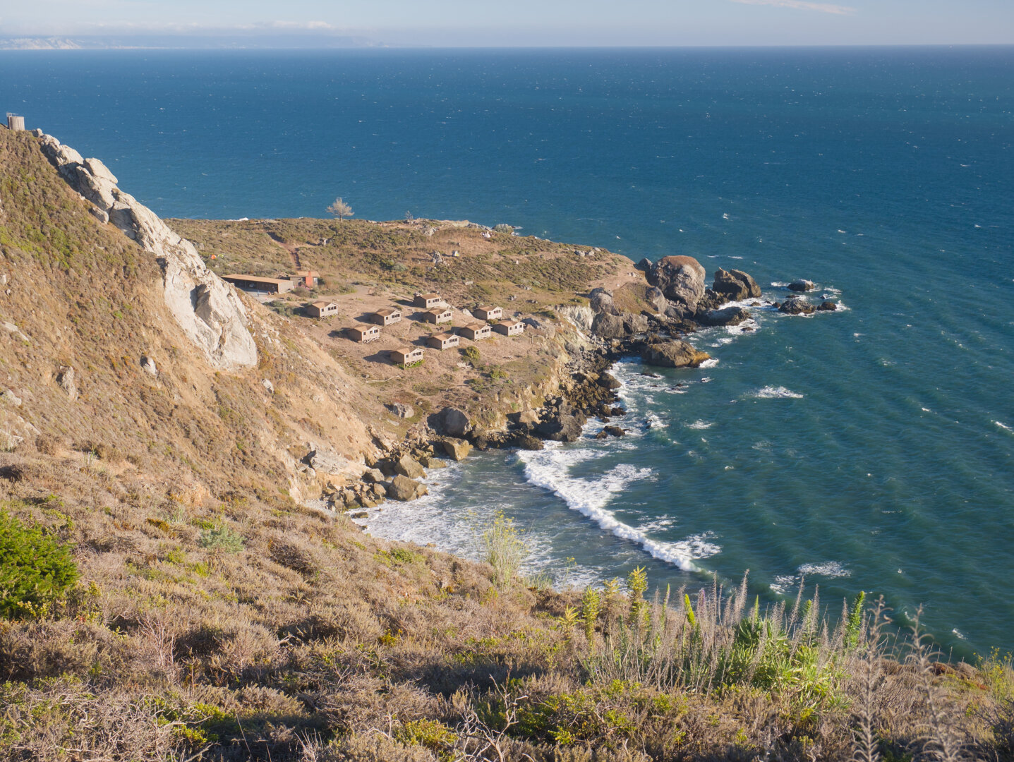 Looking down at a little peninsula in the ocean with many wooden houses for glamping