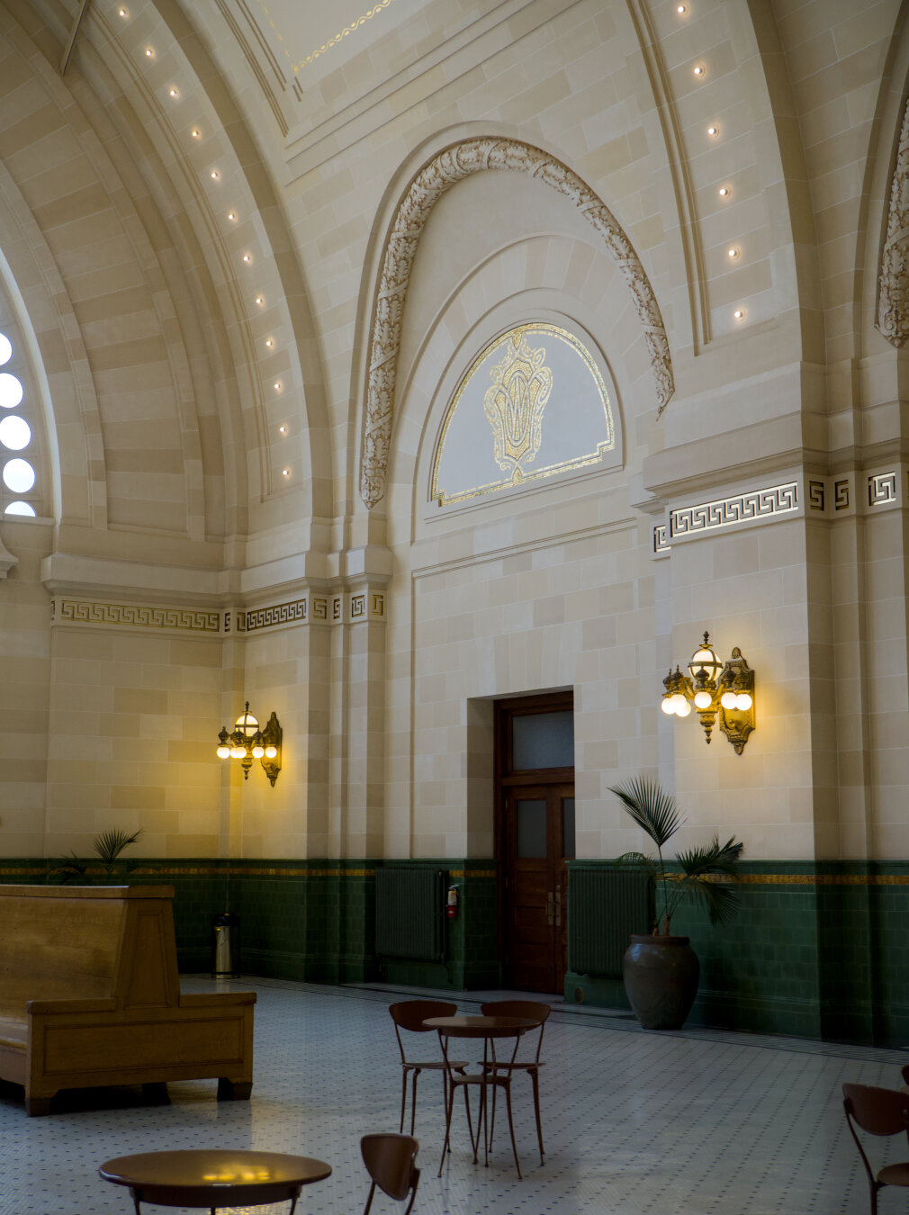 Highlighting the elaborate gold leaves at the base of the vault. The yellow lights are reflected on a small table in the foreground.