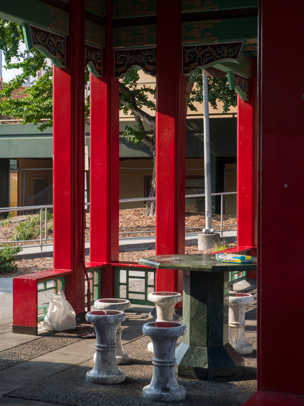 The red pillars of a Chinese pavilion, with stone stools surrounding a stone table below