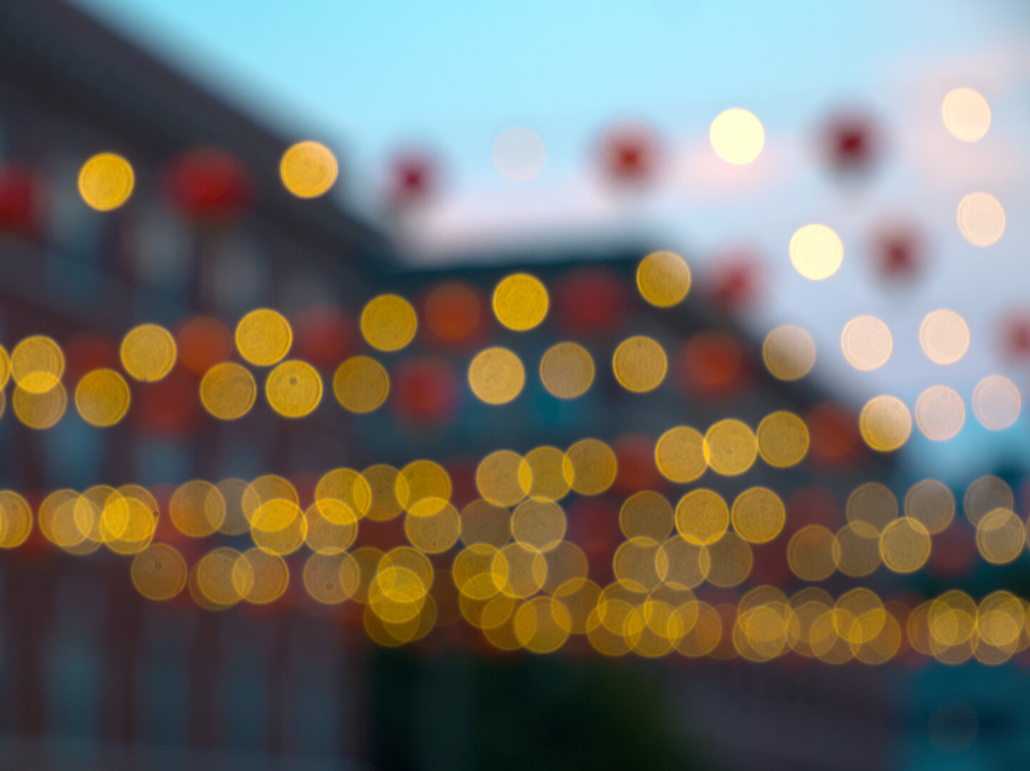 Rows of red lanterns and yellow lights are hung from buildings across King Street, just lit up for dusk. They're intentionally out of focus, so the yellow lights appear like circles and red lanterns blurry blobs.