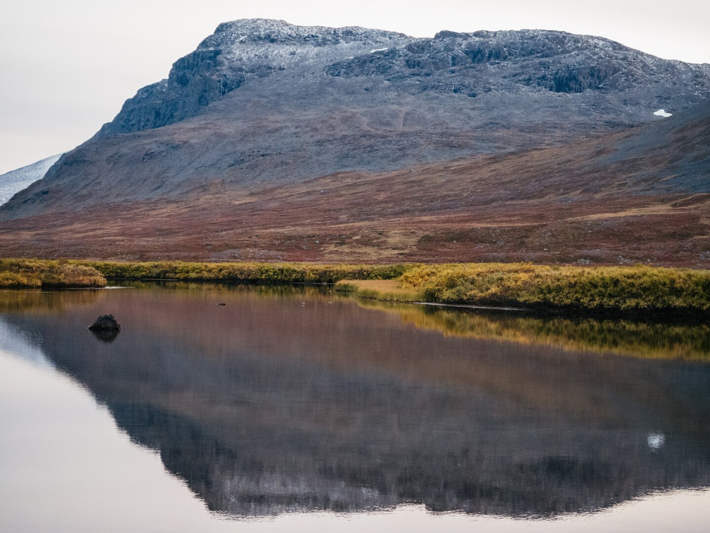 Mirrorlike lake in the foreground, with autumn colors and a mountain in the background.