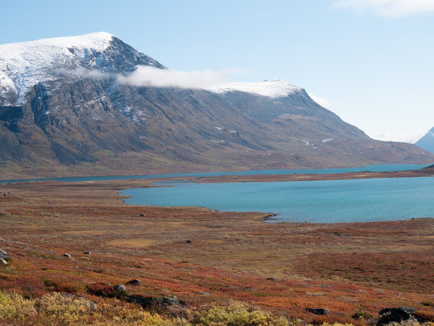 Red and orange autumn colors from bushes, snowy mountaintops, and a lake in the background.