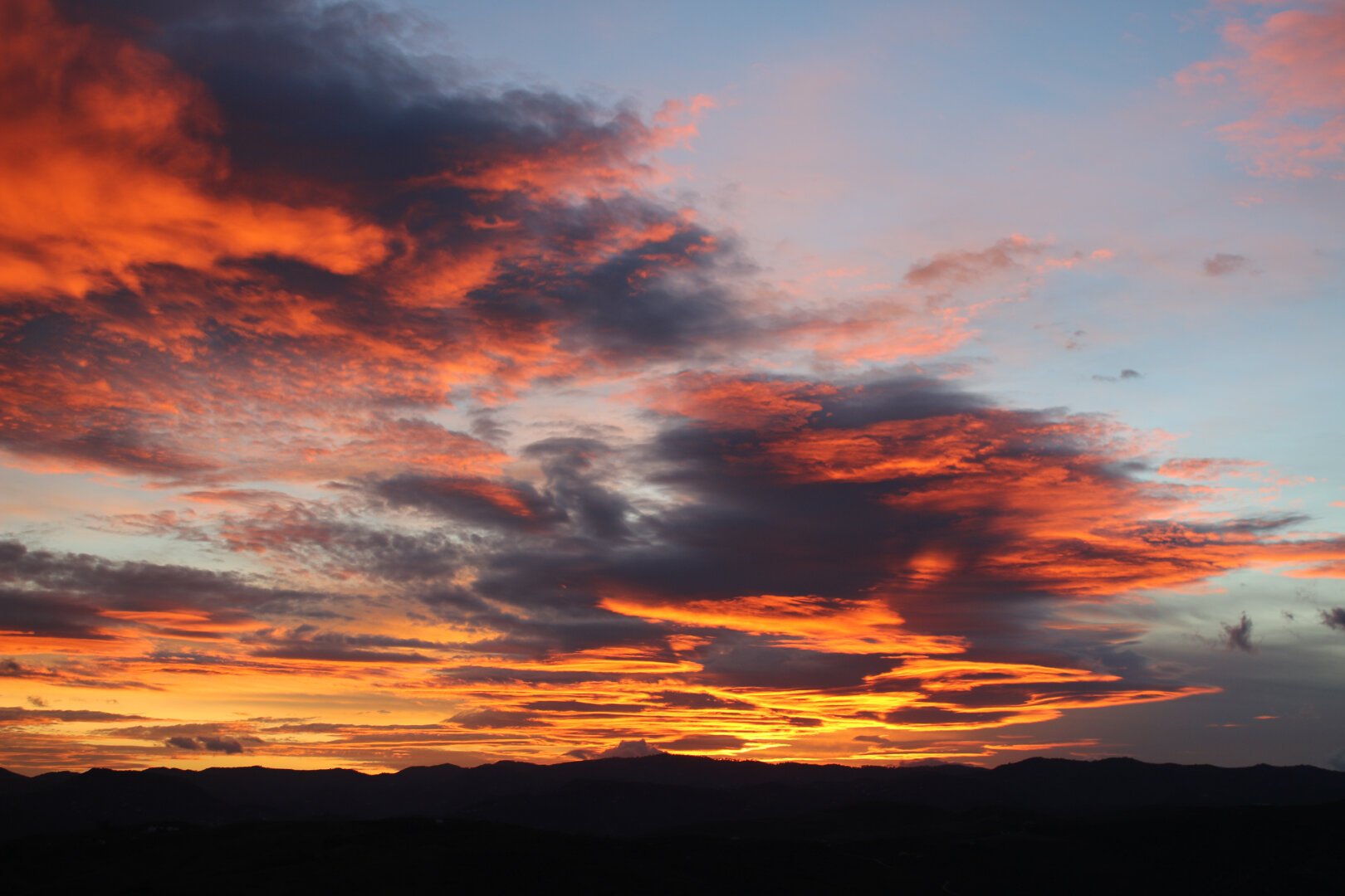 Cielo nuboso en el momento de llegar atardecer. Las nubes destacan por tener un color anaranjado bastante acentuado propio de la posición del sol, ocultándose tras las montañas.