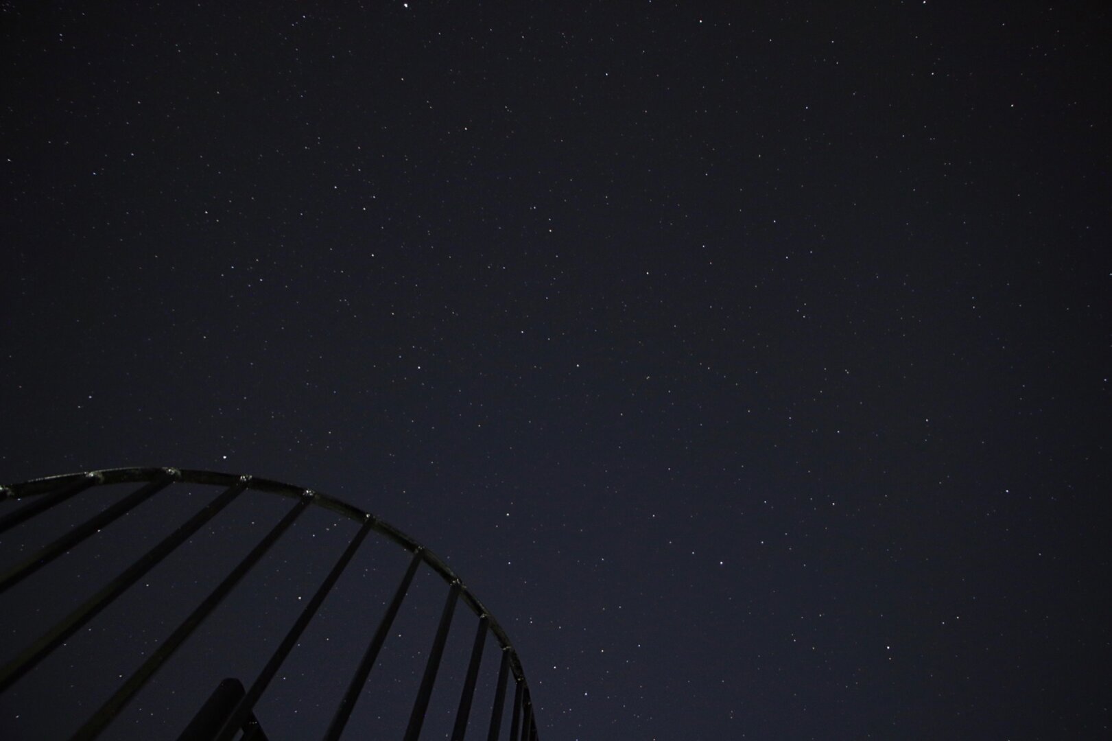Fotografia de larga exposicion en la aue se ve un cielo nocturno estrellado. En primer plano se ve parte de una escalera de caracol.