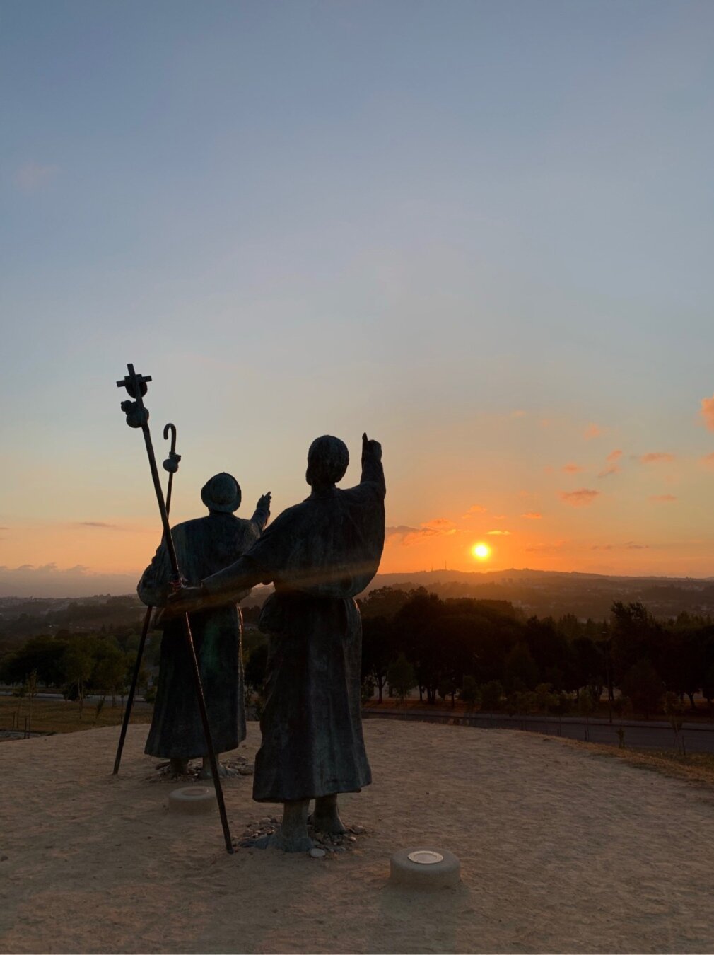 Atardecer desde el Monte do Gozo. En primer plano se ve la estatua de dos peregrunos señalando hacia el sol.