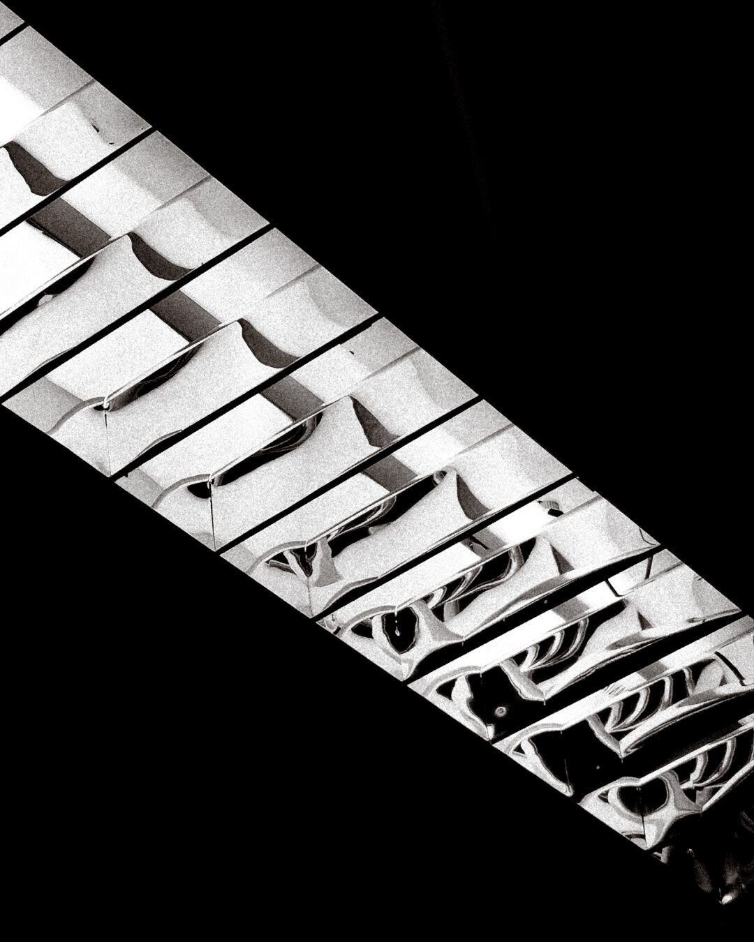 Lámpada de teito fluorescente con láminas reflectantes transversales. O reflexo é moi nítido. En branco e negro moi contrastado.