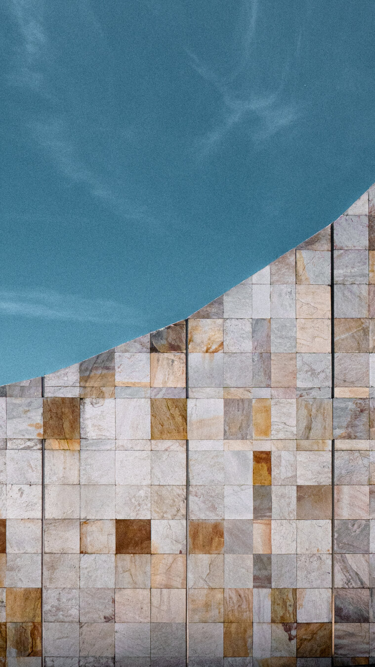 Muro de baldosas de pedra gris e marron cobroxo conta un ceo azul.