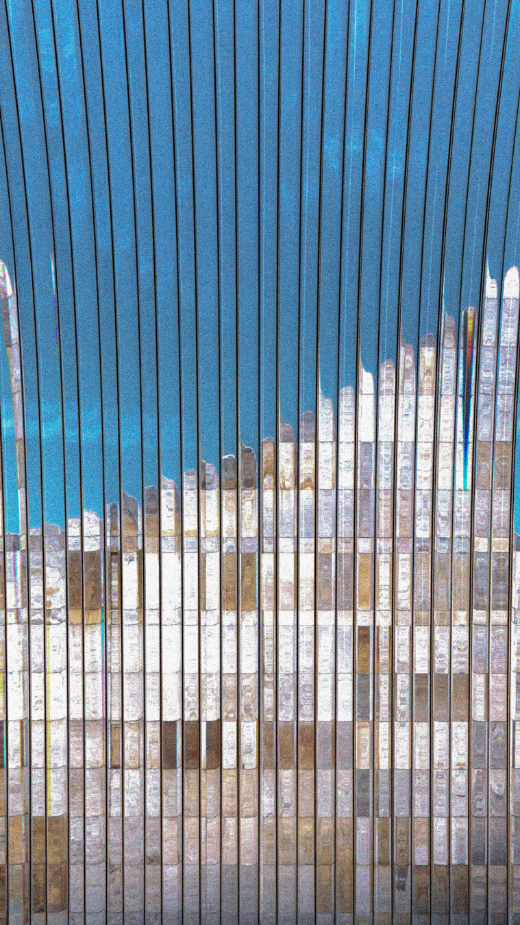 Muro de baldosas de pedra gris e marron cobroxo conta un ceo azul. Distorsionada por unha cortina de tubos de vidro.