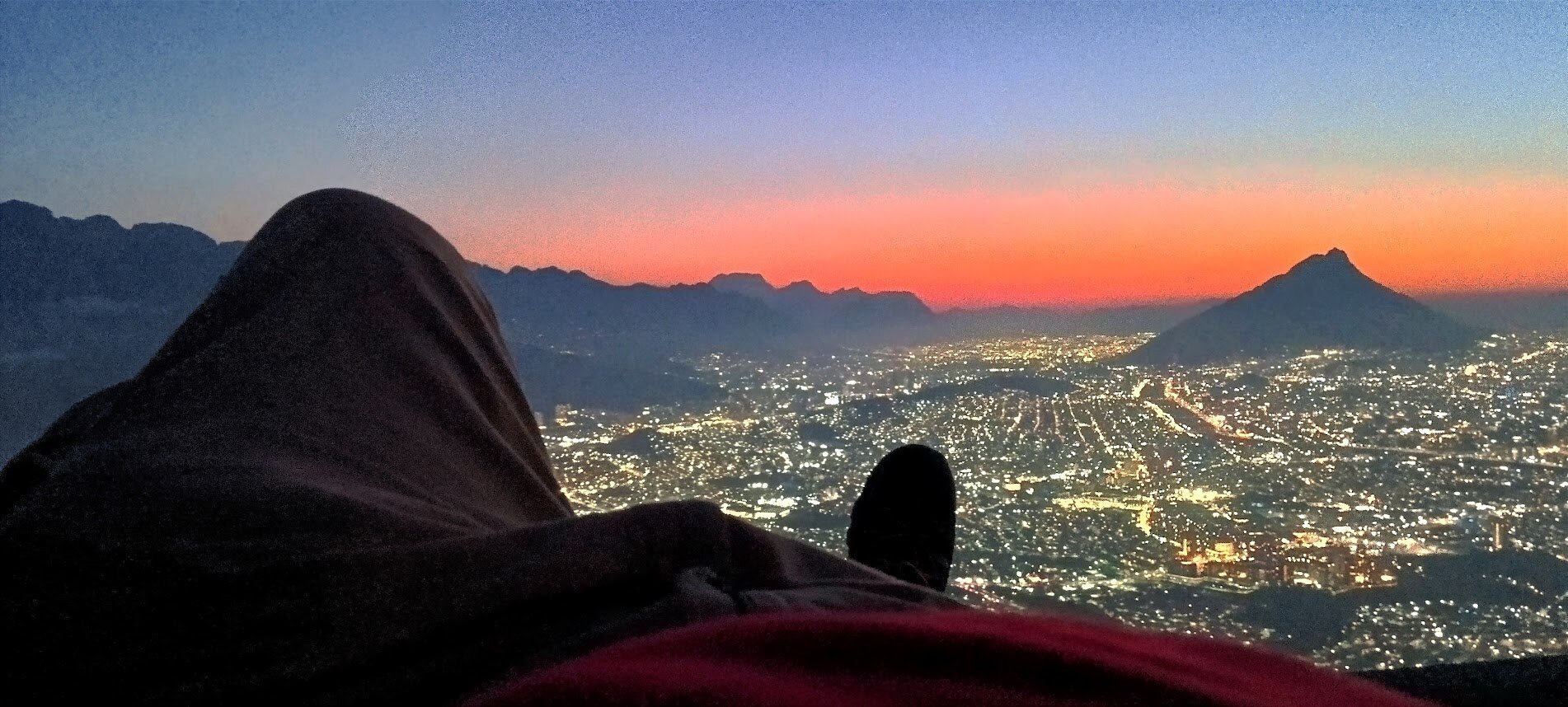 Vista del atardecer en el cerro de la silla en Monterrey, Nuevo León, estoy acostado y solo se ven mis pies, la ciudad de fondo.