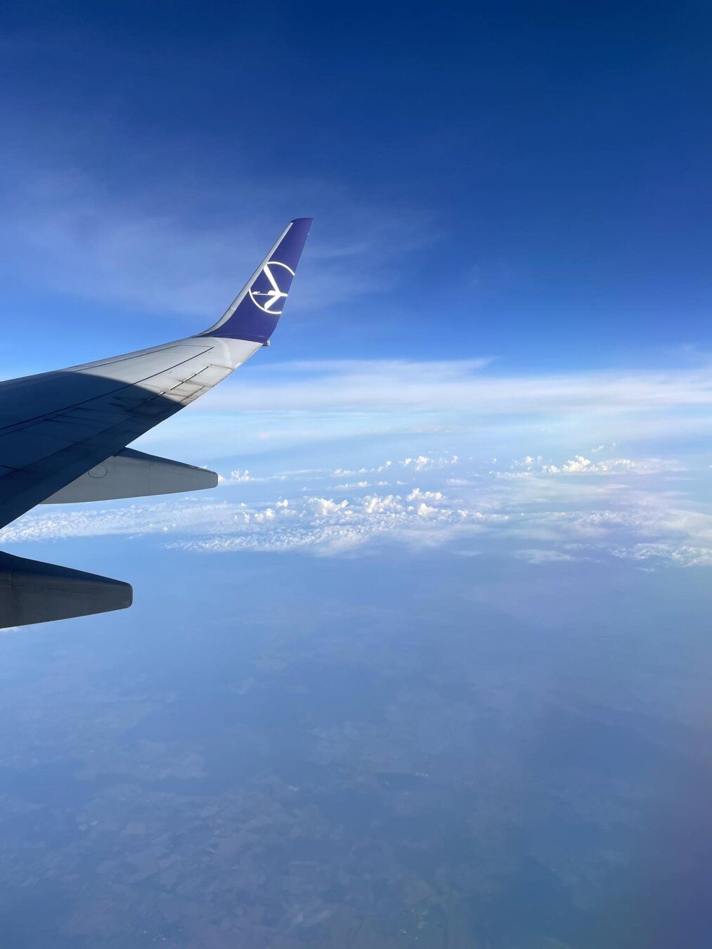 view from the window of an airplane. you can see the wingtip with the LOT logo, blue sky and white clouds