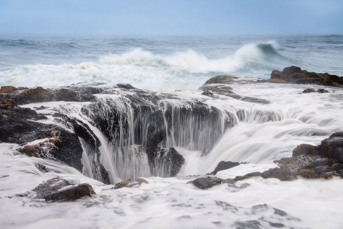 An ocean scene where the water appears to be flowing into a large hole. And, in fact, that is precisely what is happening here. This area of the Oregon coast is rocky and craggy, and has lots of these kinds of holes. This one, which is about twenty to thirty feet across, is one of the larger ones. Who knows how deep it is, but there is likely a way out at the bottom for the water. When the waves sweep in, the water pours into the hole. 

It’s also incredibly dangerous to photograph this, too. Why? Because you need to be close to it, and that means you’re out on the rocks, and any way you look at it, your back will be to the ocean. And there is, quite simply, no more dangerous position than having your back to the ocean. And that goes doubly so when you’re out on slippery rocks, close to something which is lethal, with water pouring and streaming all around you, hoping that a big wave doesn’t come in. Yeah, it was wild to create this one.