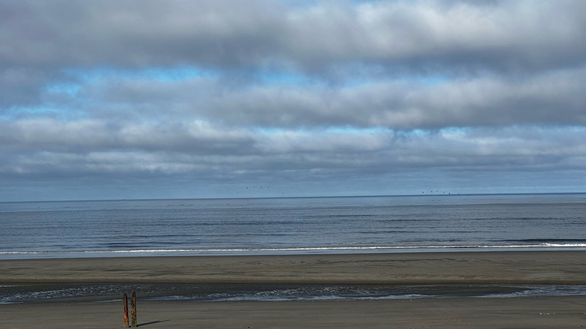 Low gray clouds with a few sunbreaks above a beach and the ocean. Waves are quite small on the ocean.