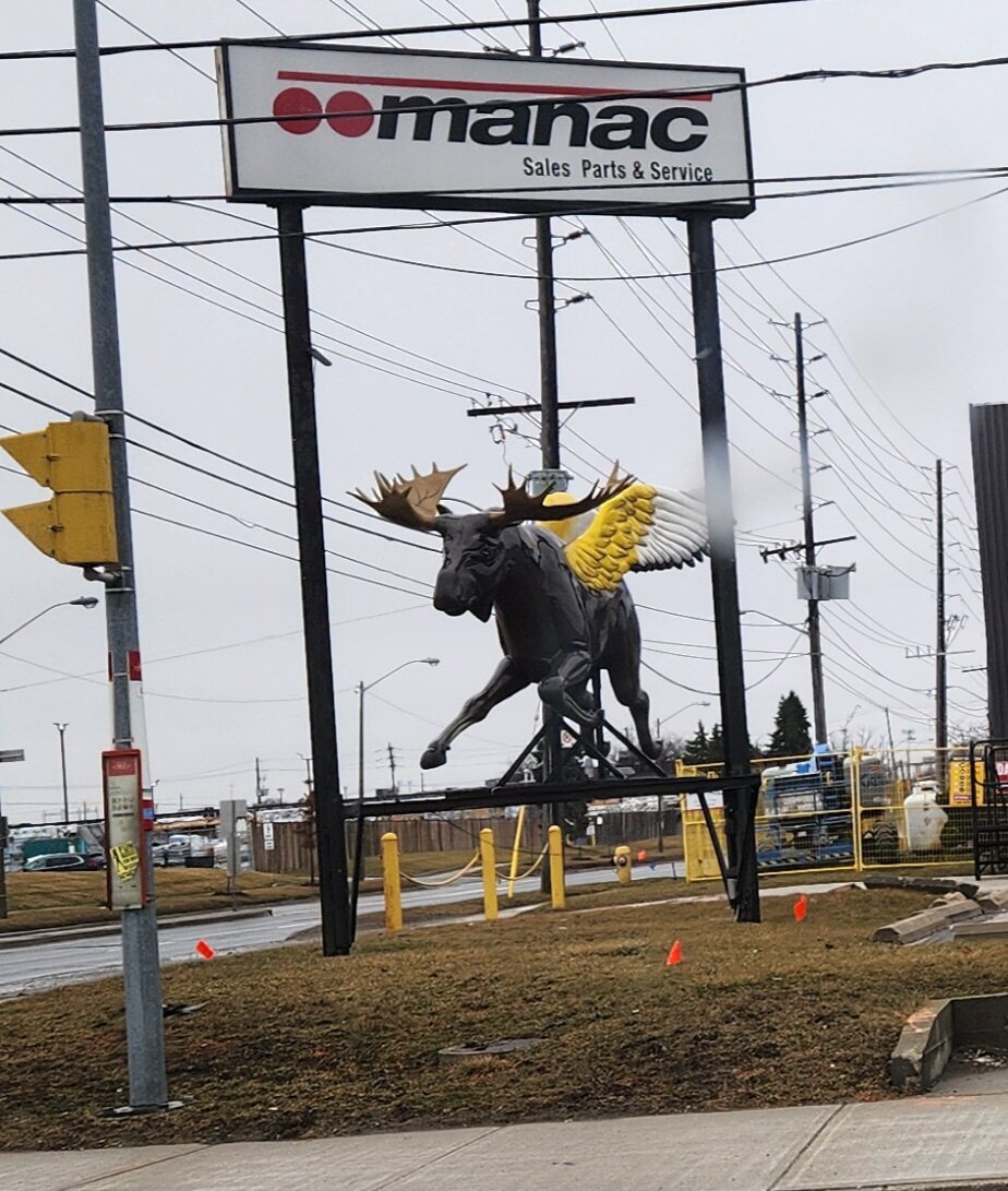 Statue of winged moose below a manac sign.