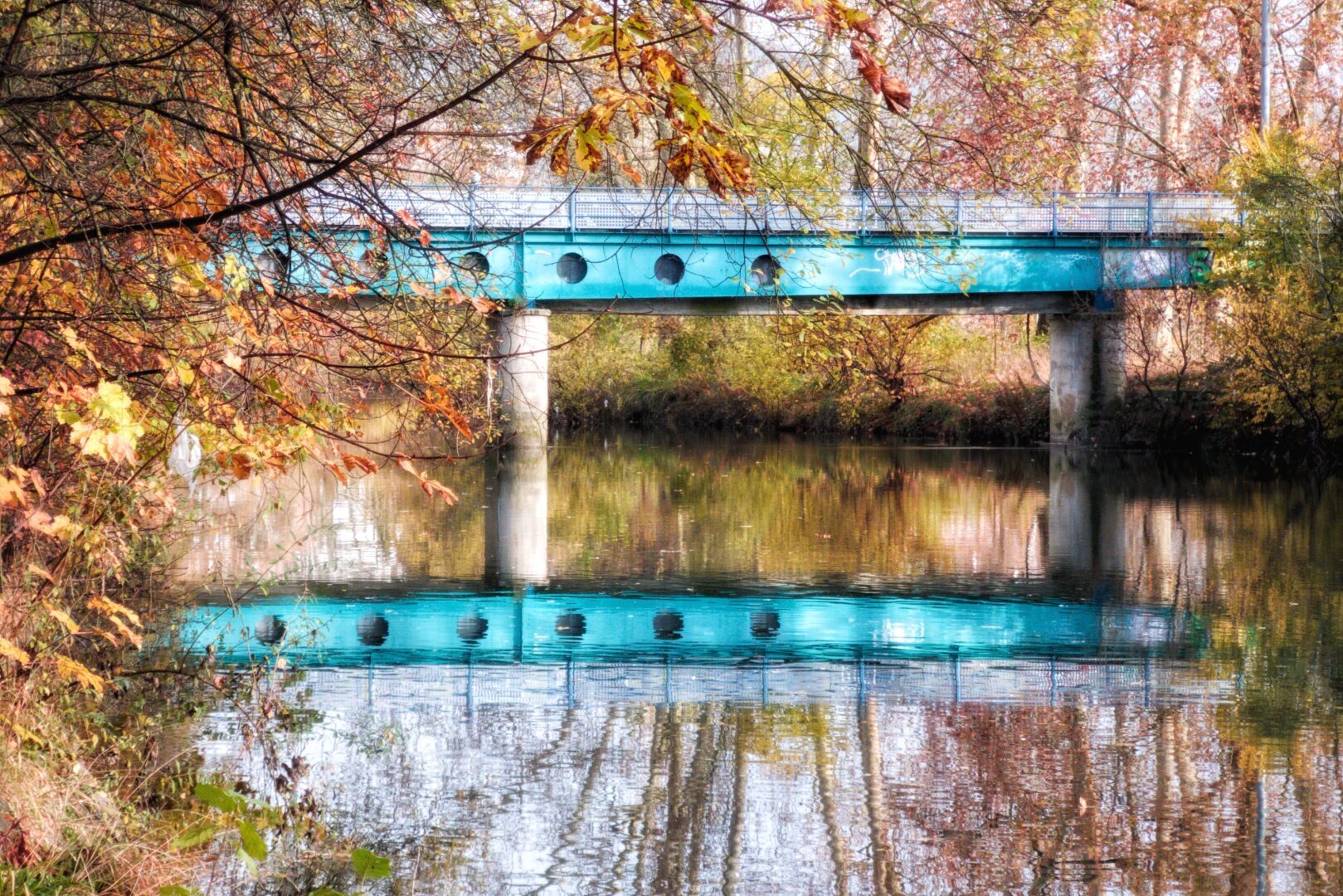 Un.puente azul se refleja en el río entre árboles otoñales.