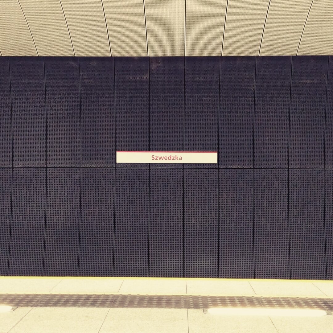 A wall in subway station with it's  name "Szwedzka" written on the sign installed on it.