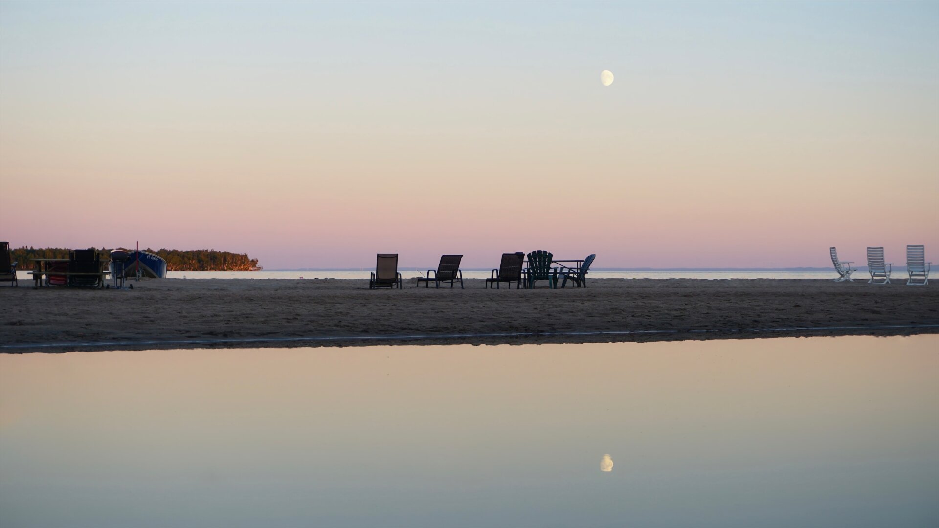 Photographie du Lac St-Jean avec des teintes de roses et bleus pastels dans le ciel. La lune se reflète sur l’eau.