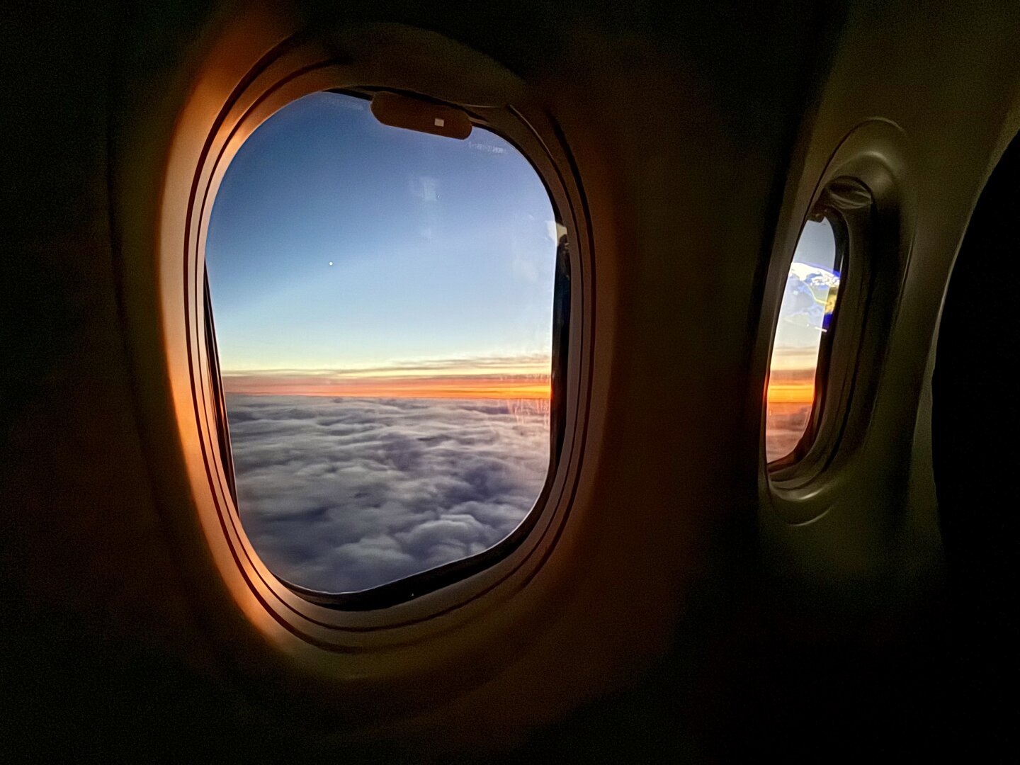 A view from inside a plane looking through two windows. You can see clouds and a sunset.