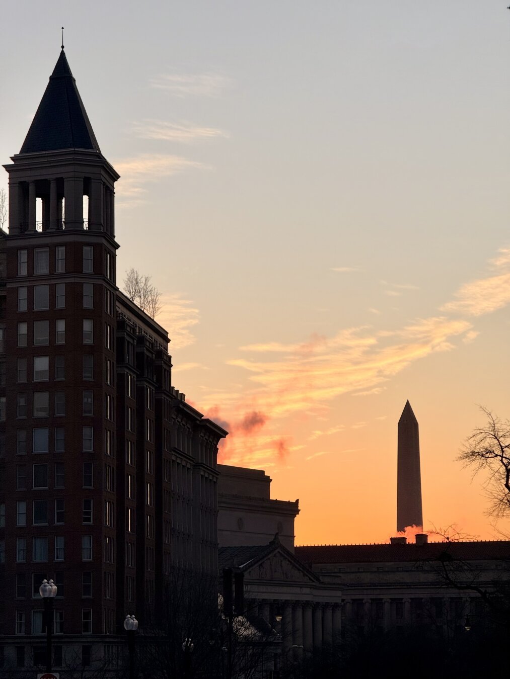 Buildings are silhouetted on the left as the sunset lights up the sky behind the Washington Monument. There’s backlit clouds of steam.