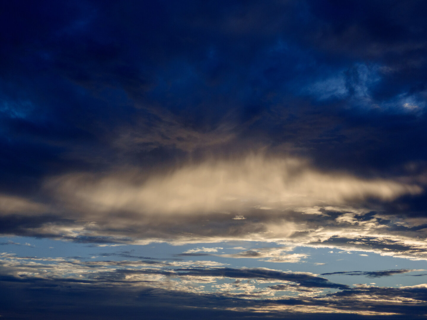 A dark, cloudy sky after sunset with one glowing cloud illuminated from below