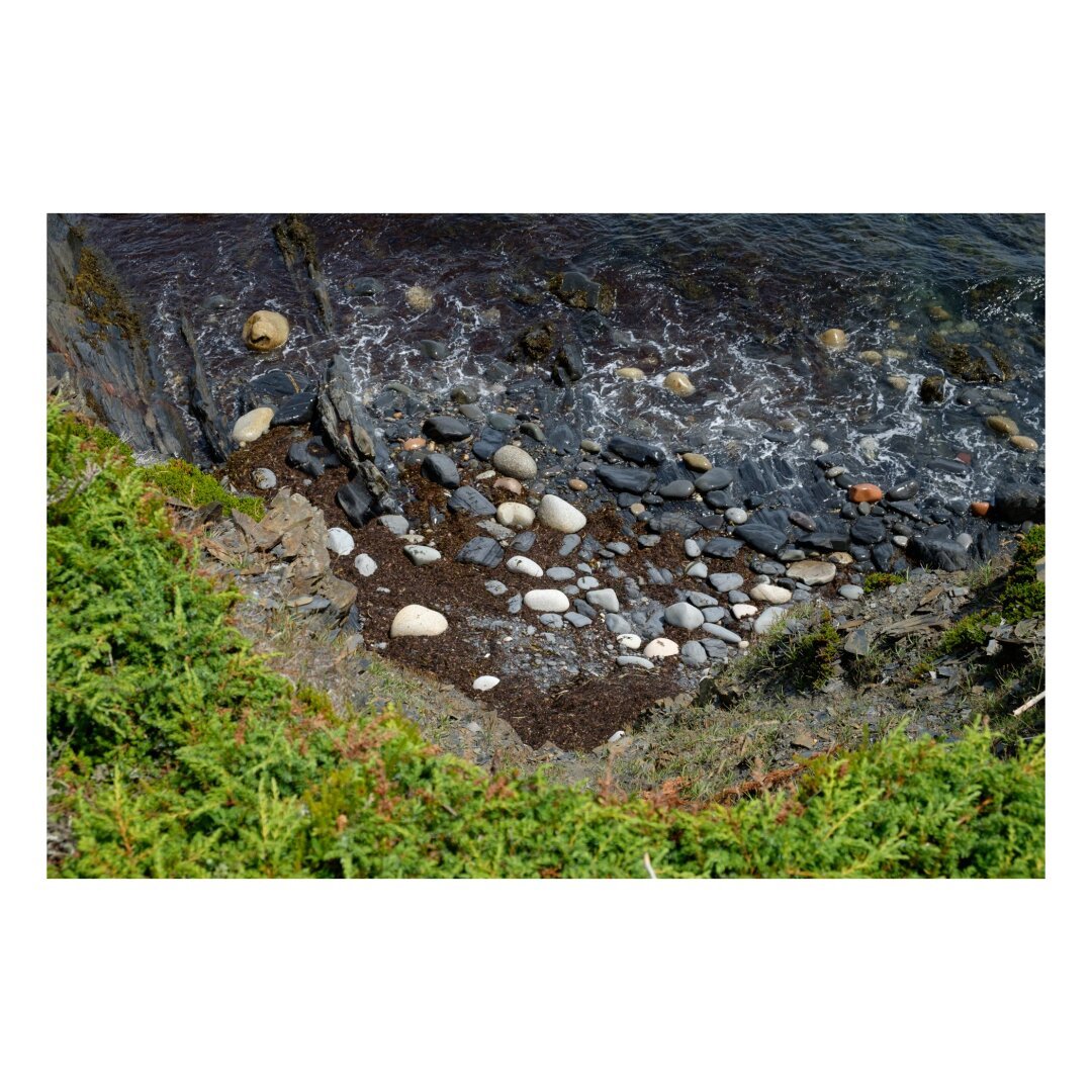 looking down from a cliff to the boulder strewn beach far below