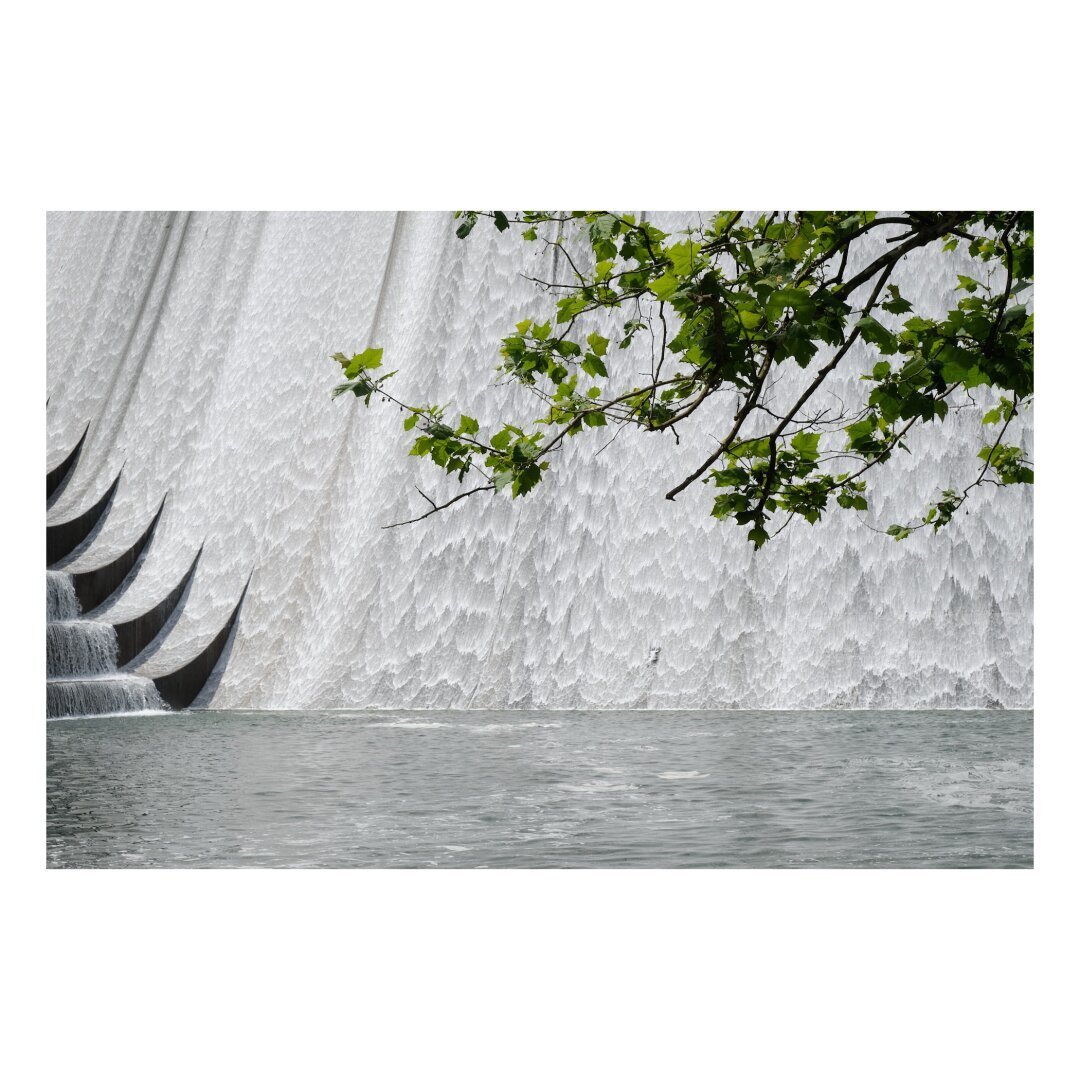 concrete dam spillways covered in veil-like wisps of water with a pond below