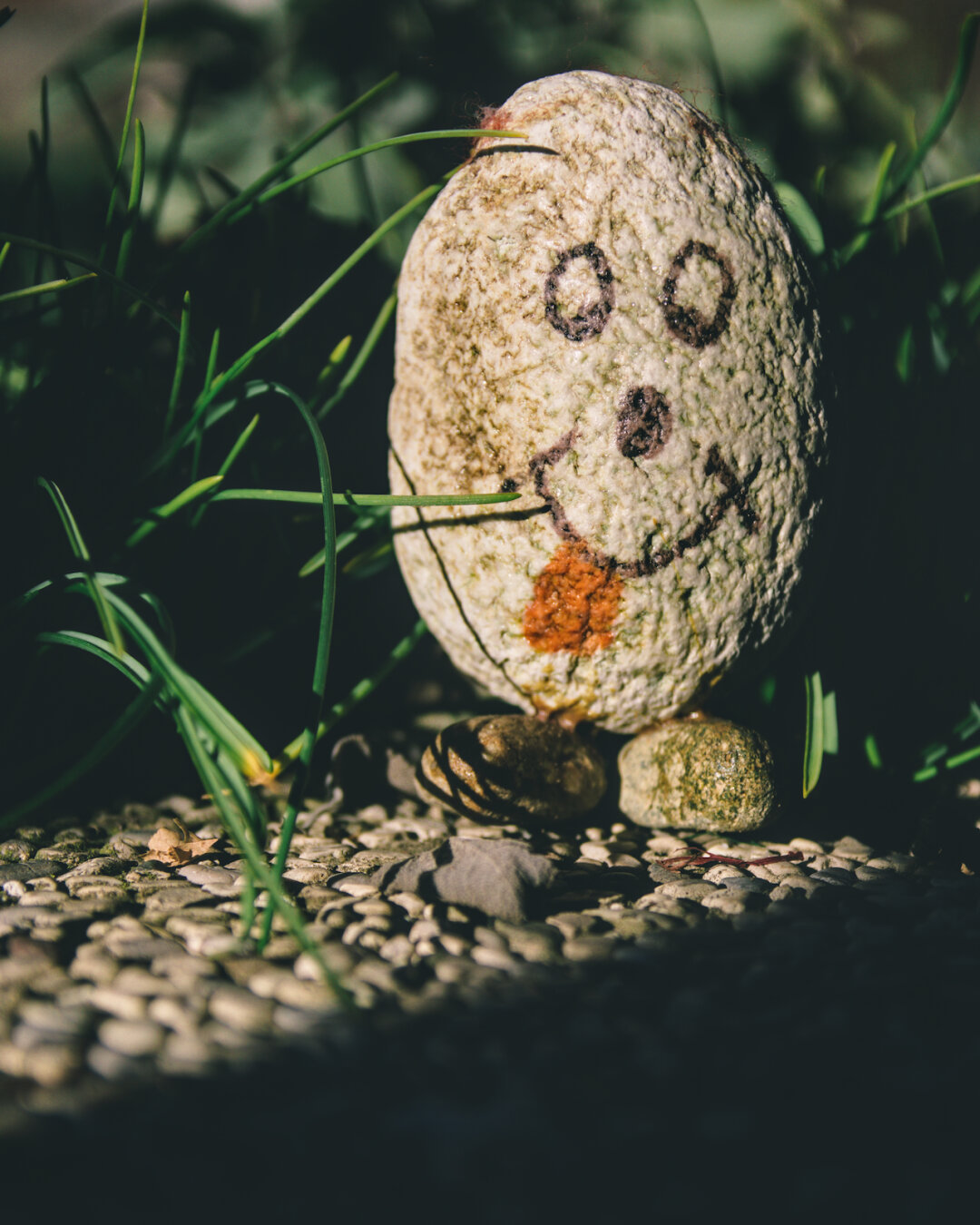 a stone with a face painted on it and two smaller stones attached at the bottom as feet