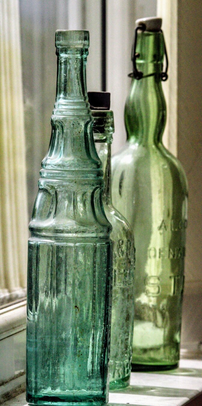 Three vintage bottles of different shades of green, in a receding line.