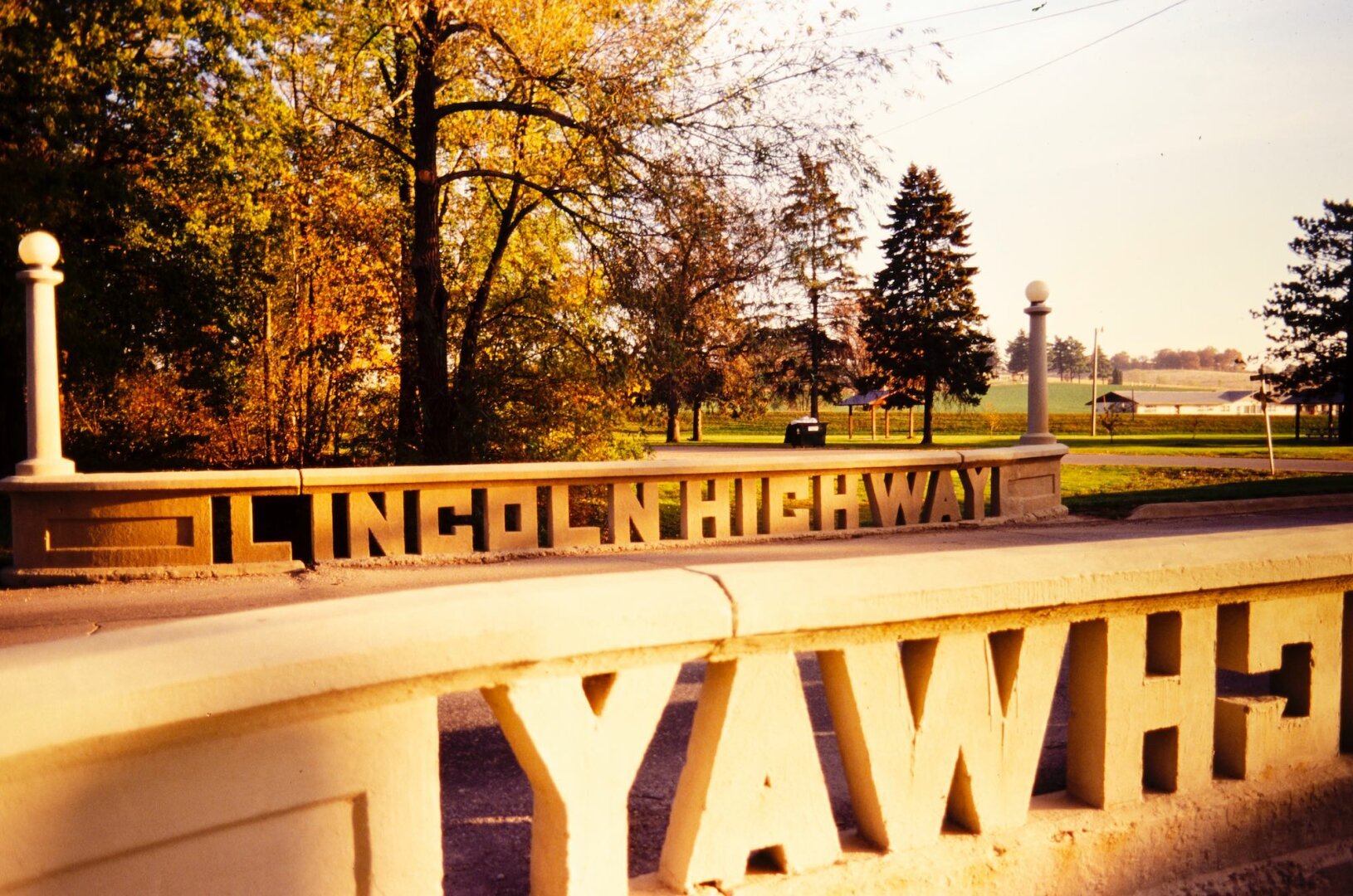 Late afternoon yellow light of a short road cement bridge. Shoulders are made with big letters reading Lincoln Highway.
