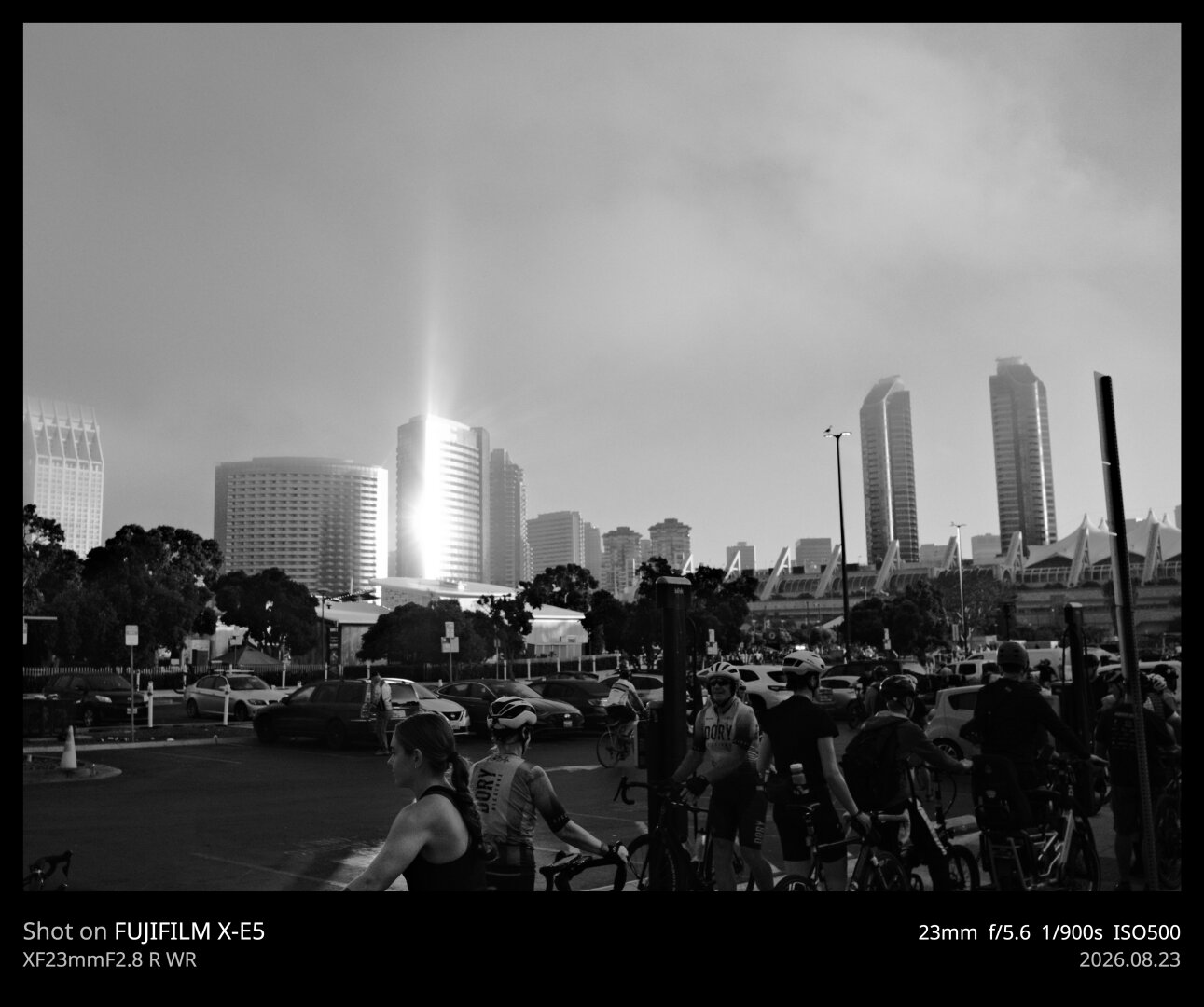 A black and white photo of a tower reflecting early morning light. In the foreground are a group of bicyclists getting ready for a big ride.