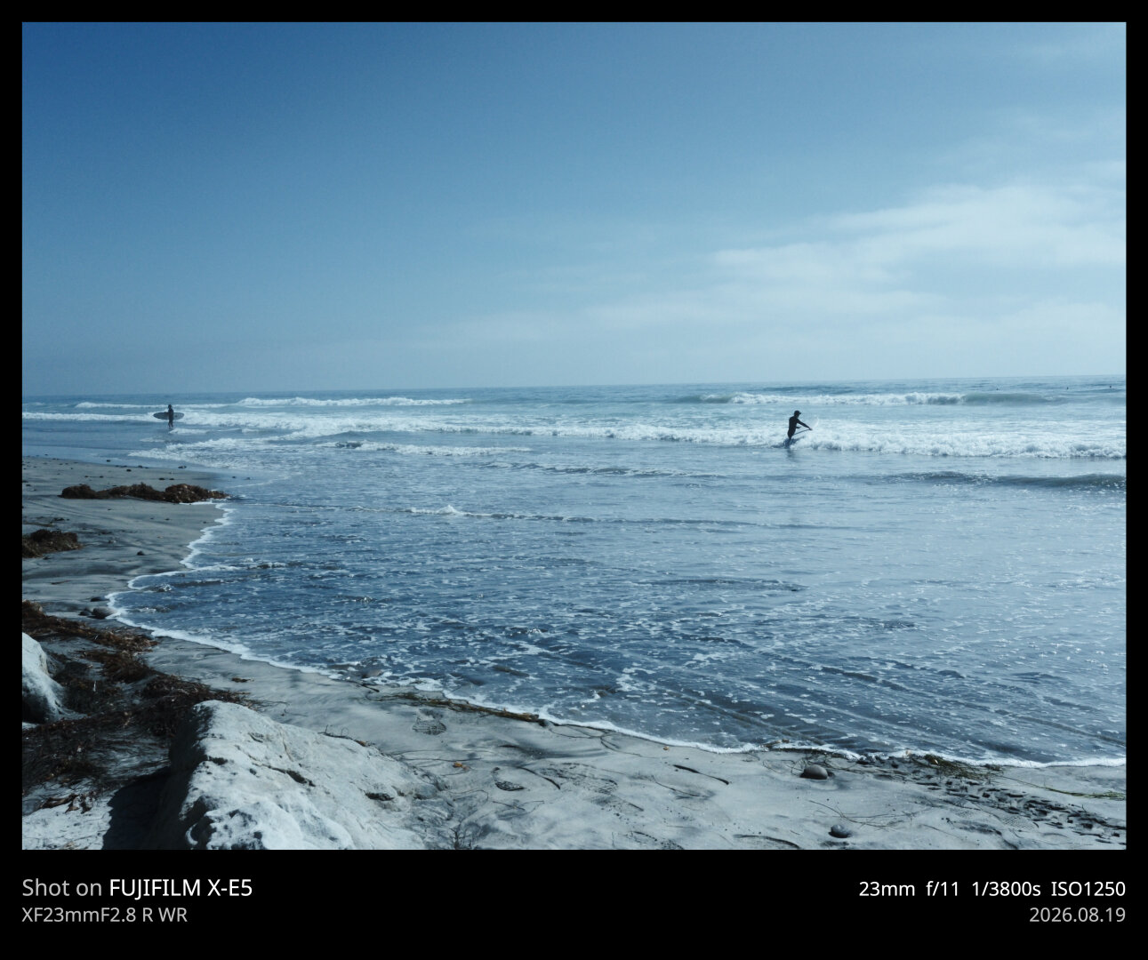 A wide shot of the ocean. One surfer can be seen getting into the water, while another is making his way out.