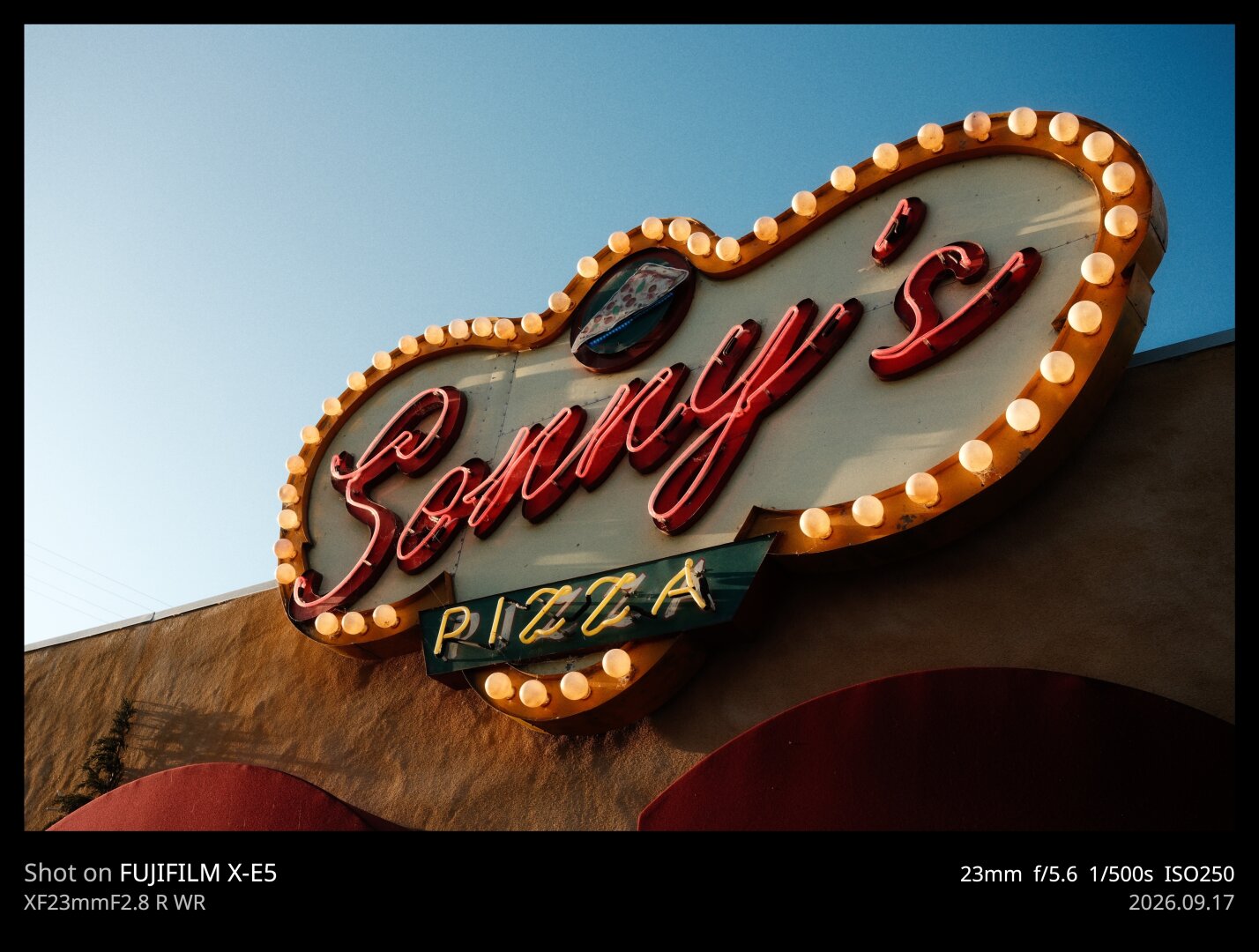 An old school pizza parlor sign reading "Sonny's Pizza." It's ringed in lights, like an old movie marquis sign. "Sonny's" is in red neon lights in a script font, and "Pizza' is underneath in yellow neon.