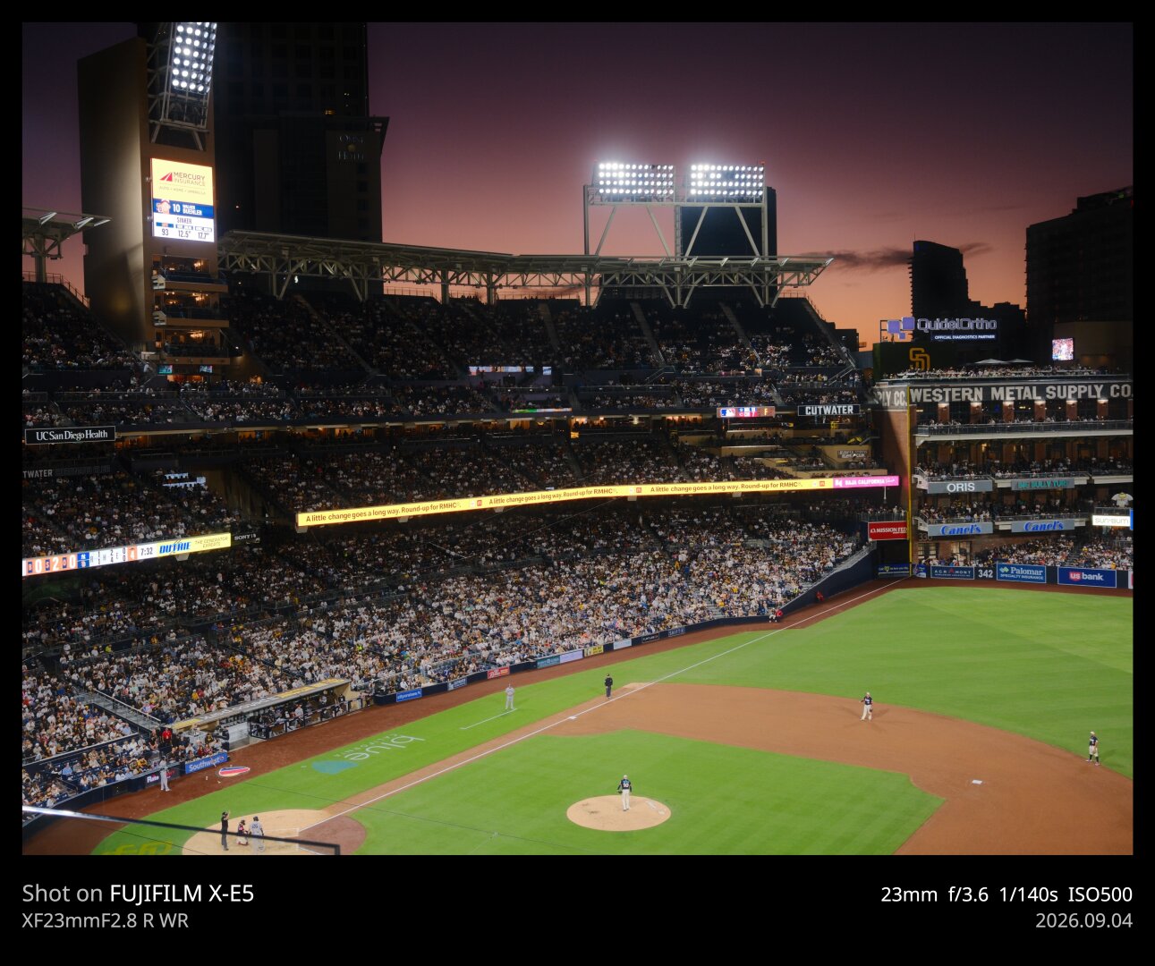 The sun has set over Padres stadium. You can see the sky still lit up in orange, pink, and purple over the first base side. The field is mostly in view as well, illuminated by stadium lights. The Western Metal Supply Co building is in view.
