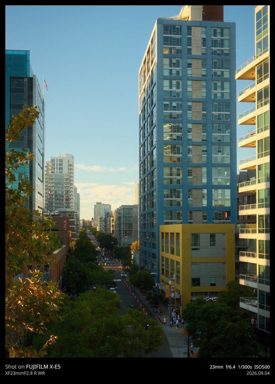 A shot taken down the Tenth Ave from the vantage point of Petco Park. This stretch of road is lined by pastel blue and yellow buildings. Then sun is beginning to set, so it's just the beginning of golden hour, which is amplifying the pastel pallet.
