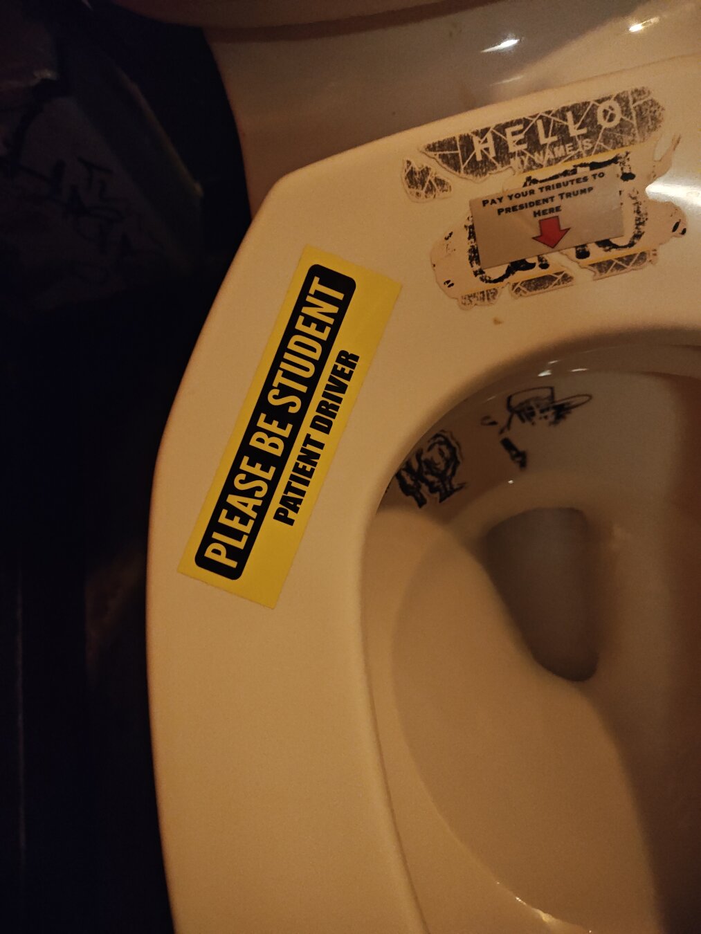 a sticker on a toilet seat which reads, "please be student. patient driver"