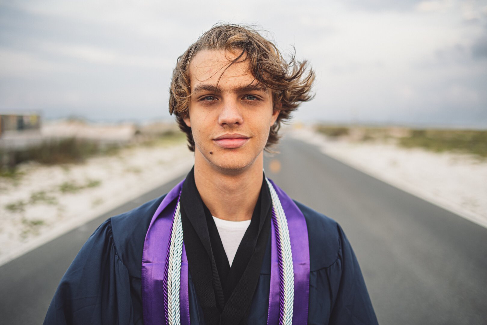 A recent graduate in robes on a street on the beach.