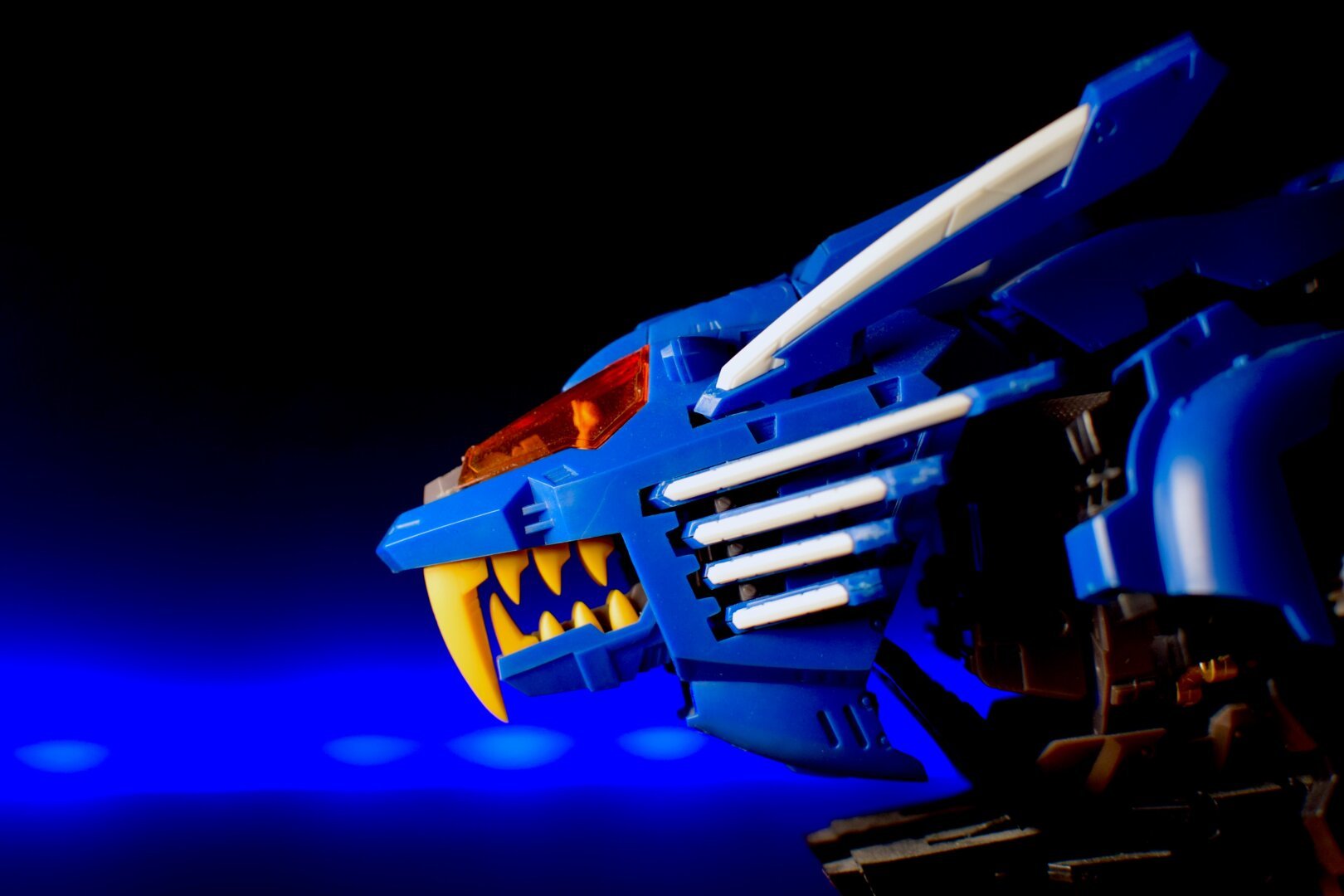 Close-up of a blue and yellow toy robot with a feline-like head against a dark background with blue lighting.