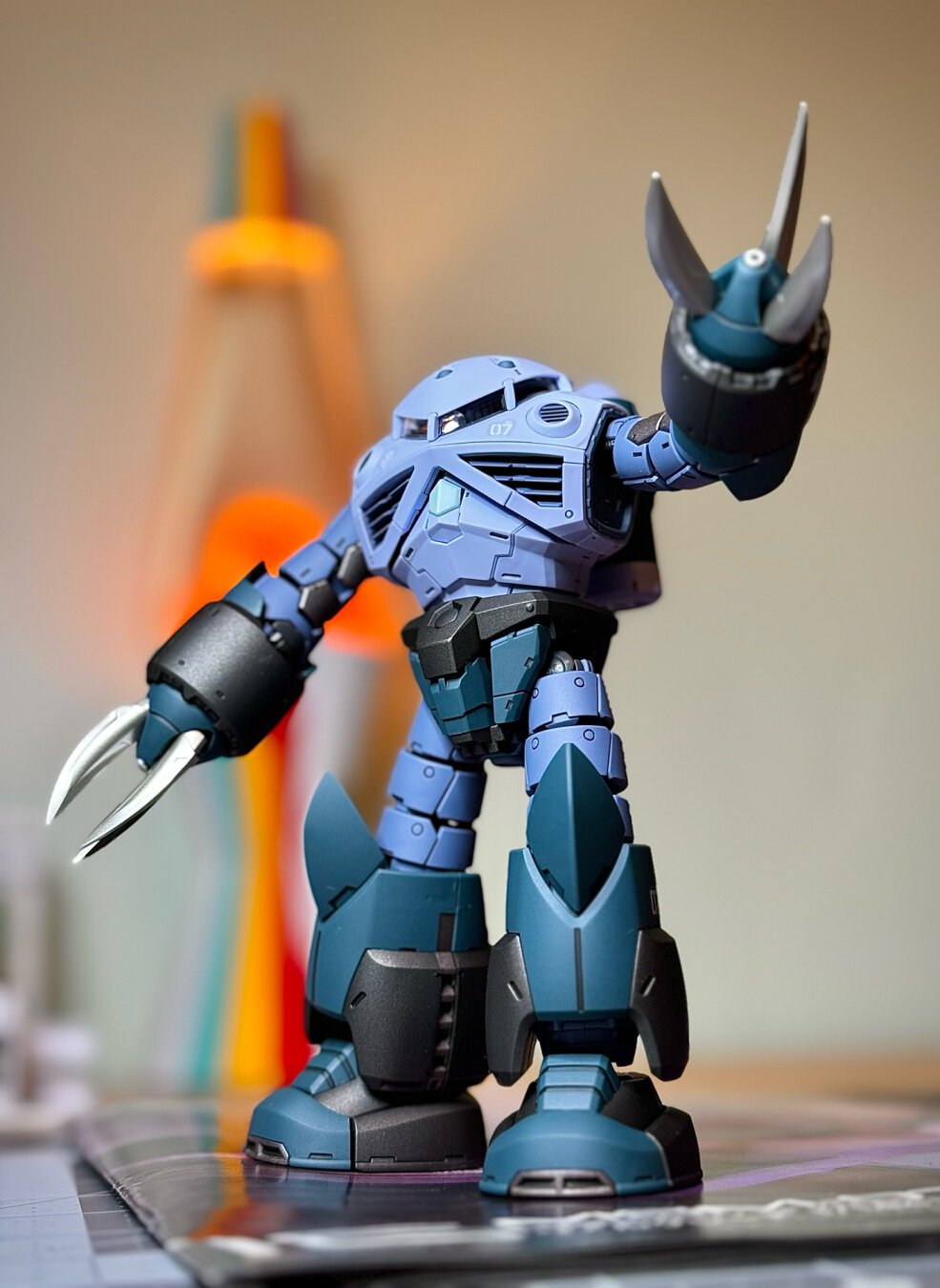 A Gundam model kit standing with one arm raised. The background is blurred slightly.