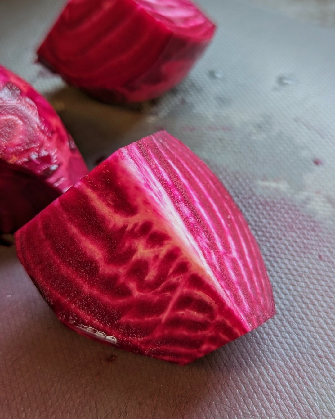A cut wedge of a beet that is deep pink with white stripes inside.