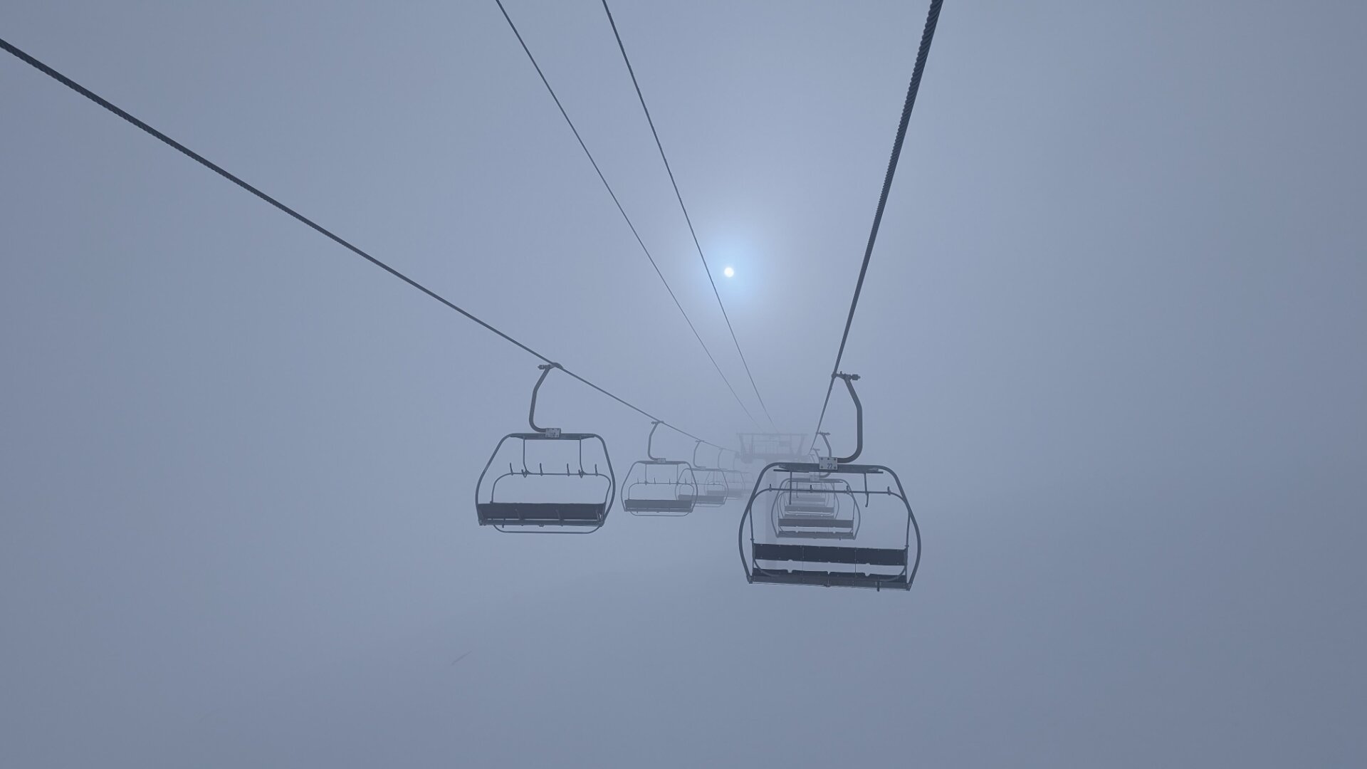 A ski lift up into the clouds. The sun is barely visible. There is no end in sight.