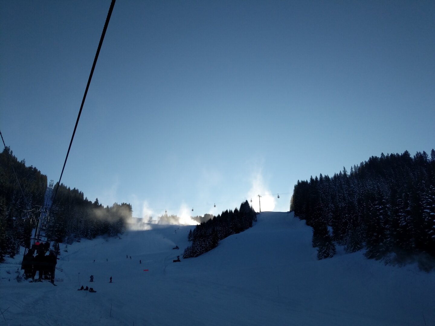 light hits the spray from snow making machines on a ridge from behind