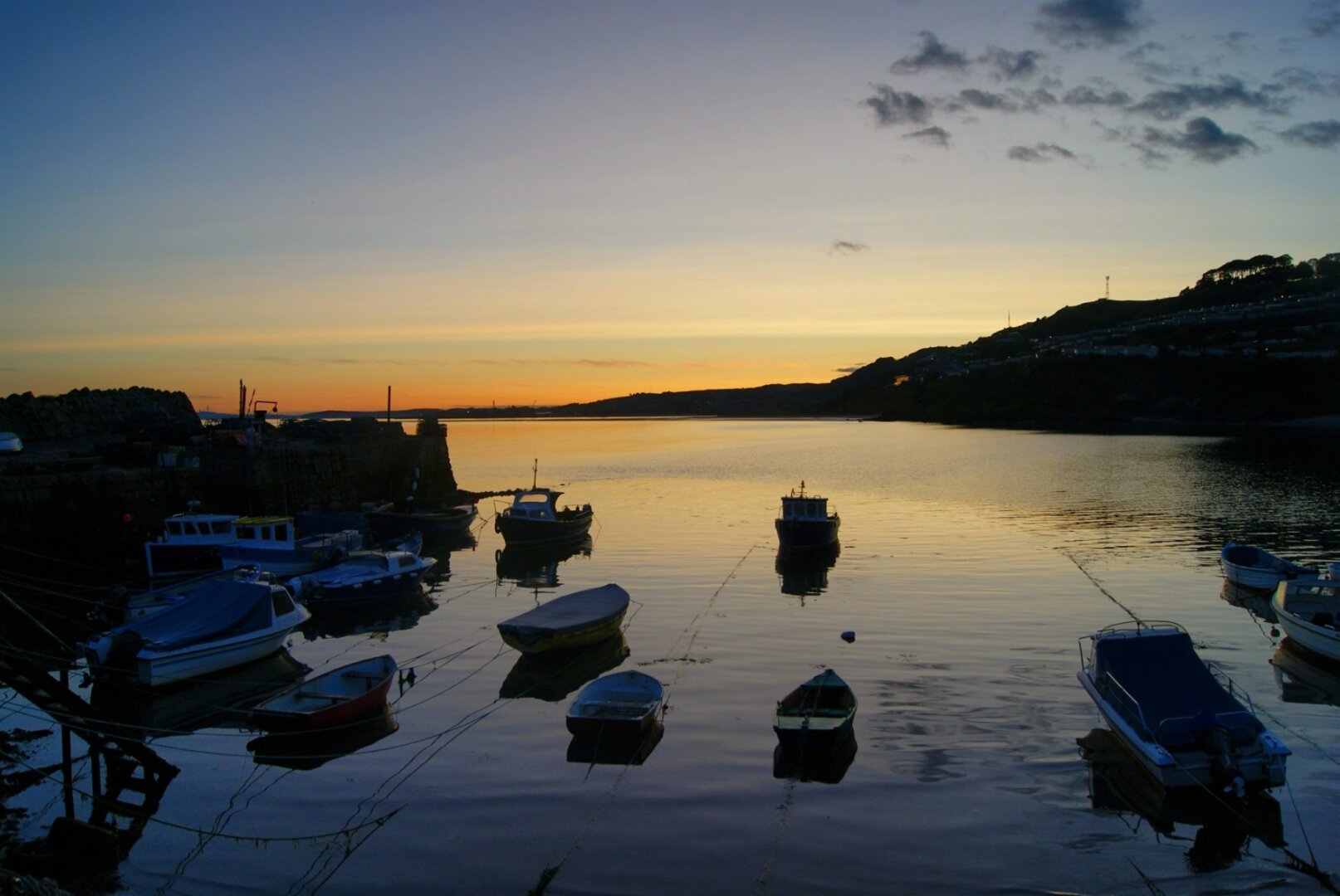 It's getting dark and there are boats floating on an almost still tiny harbour. The sea is reflecting the colours of the sunset sky.