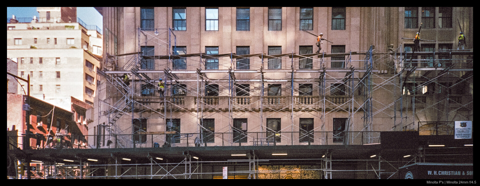 Construction workers busy themselves atop scaffolding many stories tall, passing through and between the various bars while working on a building fasade.
