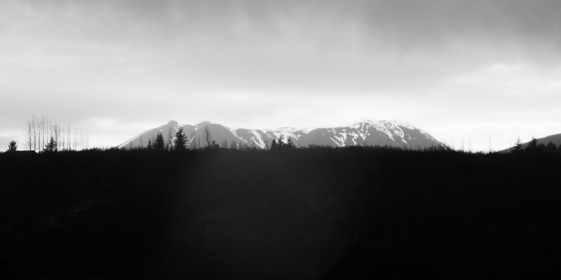 A black and white landscape at the end of the day, a snowy mountain top in the distance appearing in the horizon.