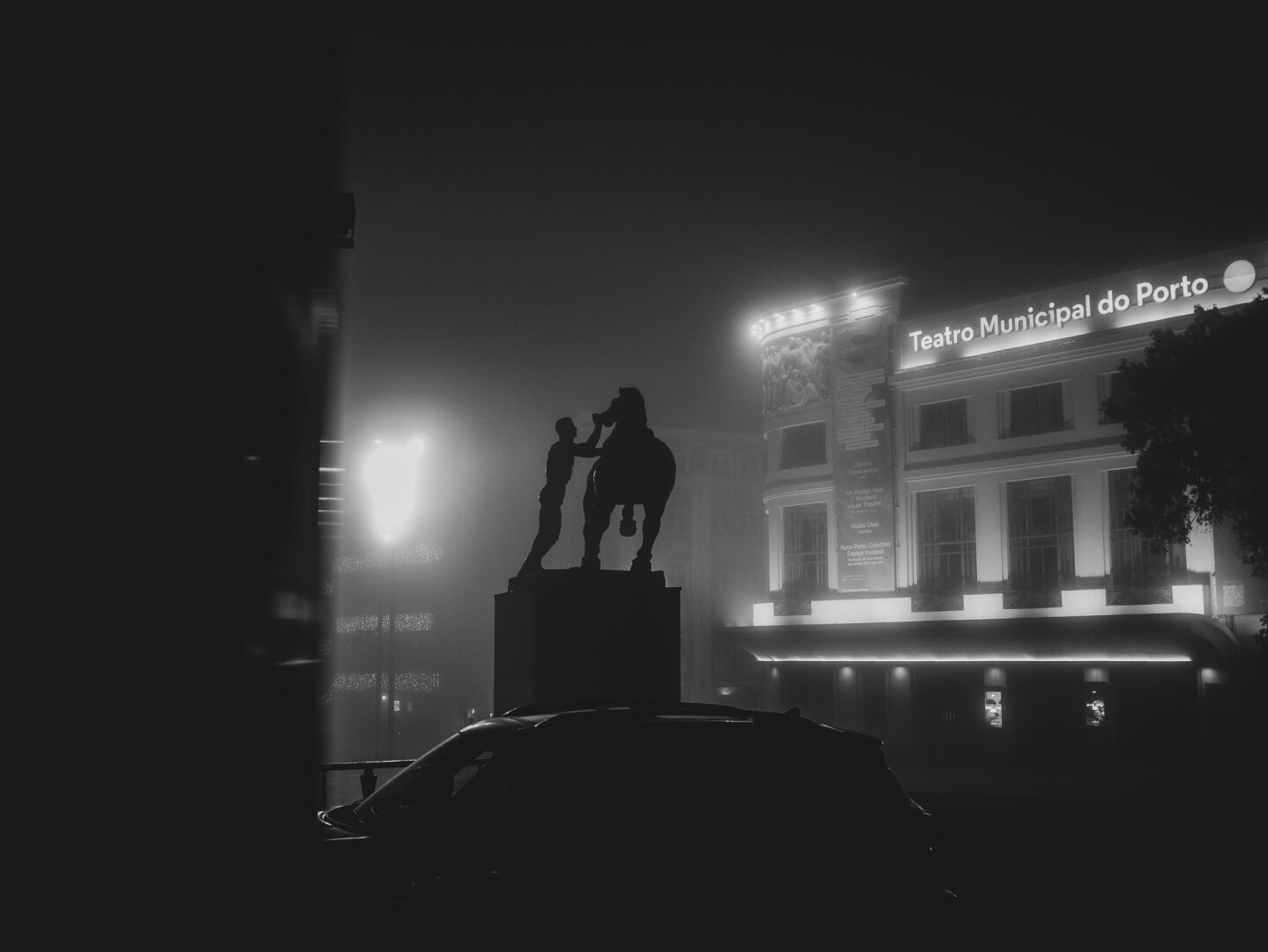 Black and white picture of a statue of a man on a horse in a square in Porto, during a foggy night.