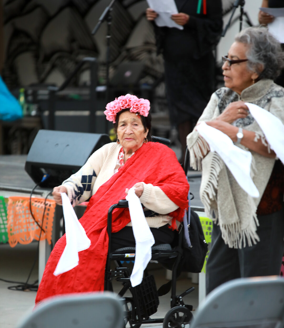 Senior person sitting in a wheelchair, but still performing the handkerchief dance with her friends. She wrinkled but happy.